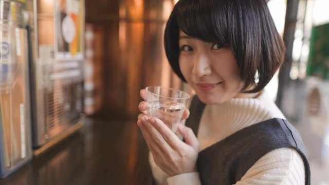年轻女子在站着的“Tachinomi”酒吧喝日本“Saki”米酒视频素材