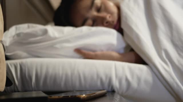 亚洲妇女疲倦困在床上，并在早上关闭闹钟的声音。视频素材