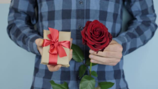 男人正对着相机展示礼物盒和红玫瑰。手握礼物为圣瓦伦丁节或国际妇女节。男正用系着红色蝴蝶结的礼盒送礼物，近距离看视频素材