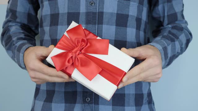 在情人节或生日这天，男性的手正在展示带有红色丝带蝴蝶结的礼盒。男人拿着系着蝴蝶结的礼物，在手里摇晃着。圣诞节的节日礼物视频下载