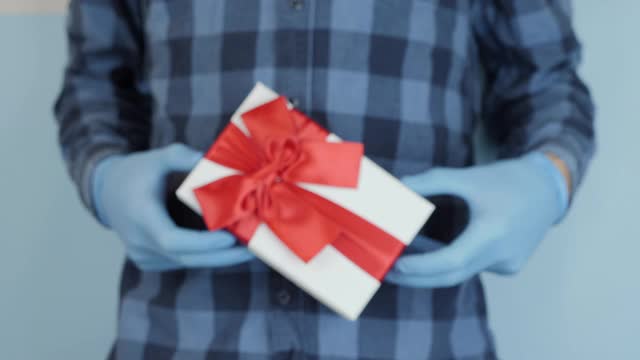 情人节和假日庆祝活动。男性手拿医用橡胶手套正在展示带有红色丝带的礼品盒。男人拿着一个带红色蝴蝶结的礼盒视频下载