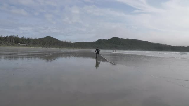 慢动作，一个冲浪者与一个沿着海滩走的板的后视图，温哥华岛视频下载