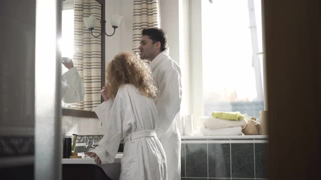 正面的白人夫妇早上在家里刷牙的侧视图。白种人丈夫和妻子在室内浴室照顾健康。卫生和日常生活概念视频素材