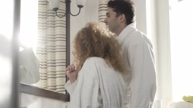 健康的白种人夫妇在浴室镜子反射的阳光下刷牙。正面的观点，男人和女人照顾健康在早上在家视频素材