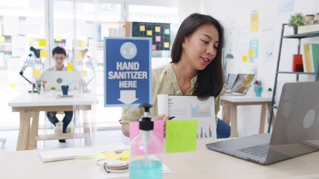 亚洲商界女性在新常态下保持社交距离以预防病毒，同时在办公室使用笔记本电脑向同事演示视频通话计划。视频素材