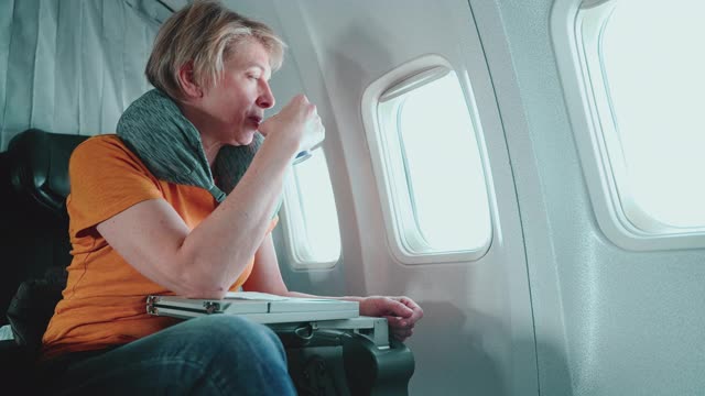 55岁的成熟女性在飞机上望向窗外。视频下载
