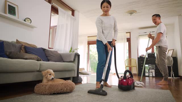 幸福的年轻夫妇女人清洁地毯与真空吸尘器机器和男人拖地在现代家庭视频素材