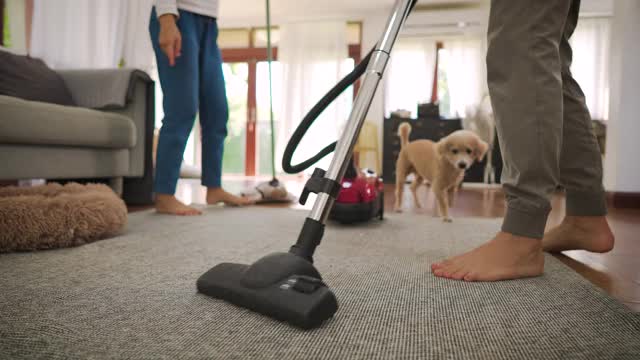 幸福的年轻夫妇女人清洁地毯与真空吸尘器机器和男人拖地在现代家庭视频素材
