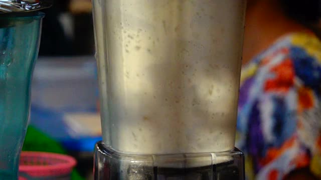 健康牛奶有机奶昔，香蕉冰沙的准备过程。在搅拌机里搅拌。香蕉和牛奶在搅拌机里混合。在搅拌机里搅拌原料的女人。视频素材