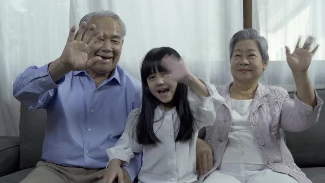 快乐的亚洲小女孩与年老的祖父母打招呼聊天与摄像头在家里做视频通话。视频素材