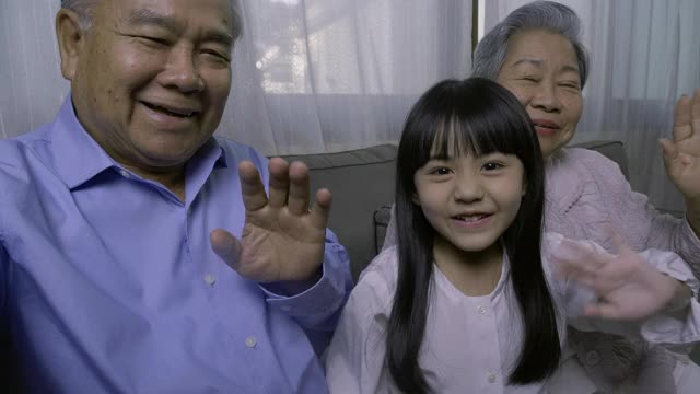 家人在视频通话，快乐的爷爷奶奶和孙女在家里一起视频通话。视频素材
