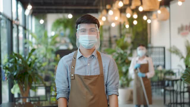 亚洲工人夫妇穿着围裙和口罩看着相机准备清洁餐厅在现代餐厅视频素材