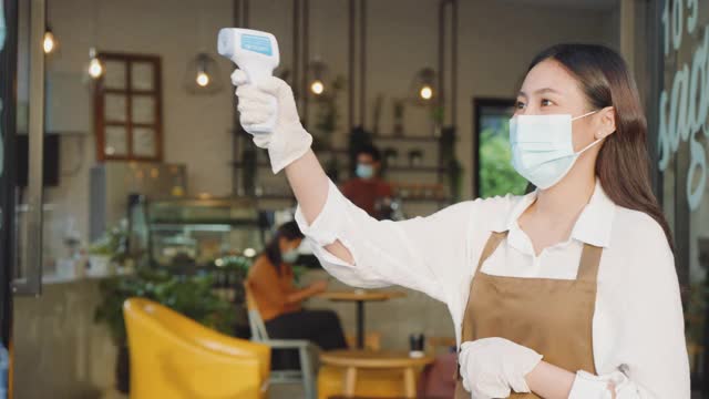 亚洲女性咖啡厅员工在量体温后戴口罩的亚洲男性在去餐厅或咖啡厅前，为了新冠肺炎大流行的正常生活方式。视频素材