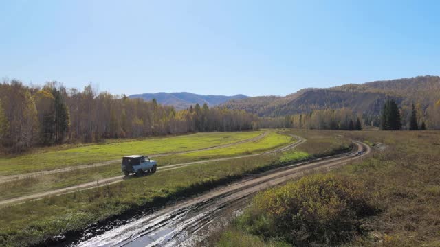 一辆汽车在田野周围的乡村道路上行驶，森林的背景是一座山，直升机在拍摄视频下载