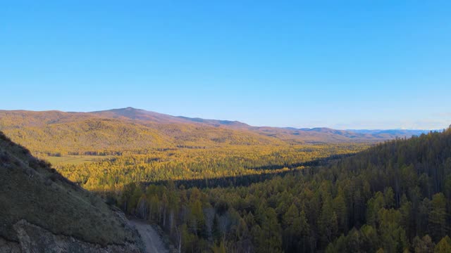 无人机飞越森林覆盖的山脉。秋天。蓝色的天空视频下载