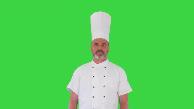 严肃的厨师与他的双臂交叉看着镜头上的绿色屏幕，色度钥匙视频素材