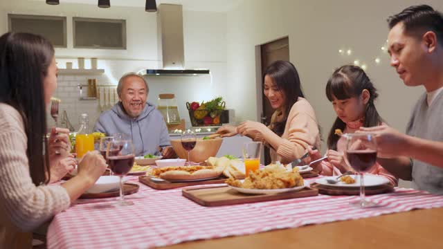 幸福的家庭时间和关系，亚洲大家庭有一个小聚会，一起在家里吃东西。爷爷很高兴看到他的孩子和侄子在家里的餐桌上吃饭，分享食物。视频下载