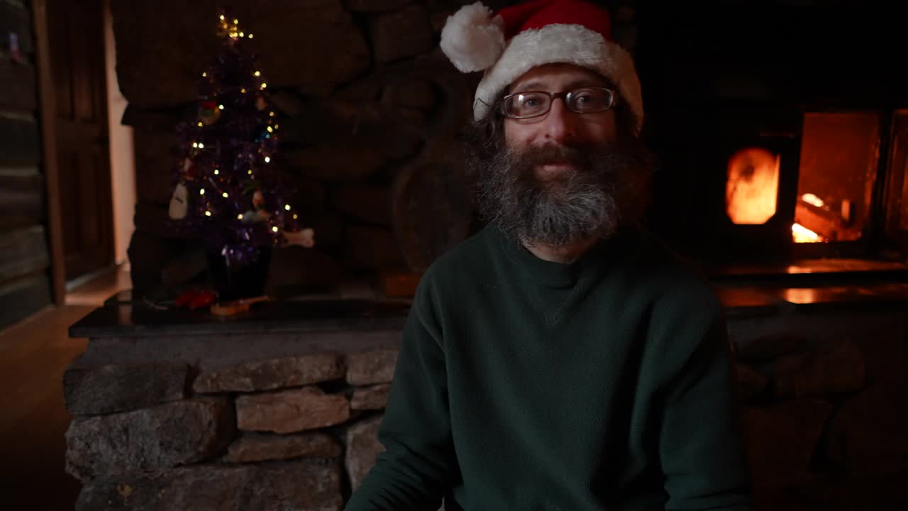 一个留着浓密胡子戴着圣诞帽的男人打开了一份里面有手机的礼物视频下载