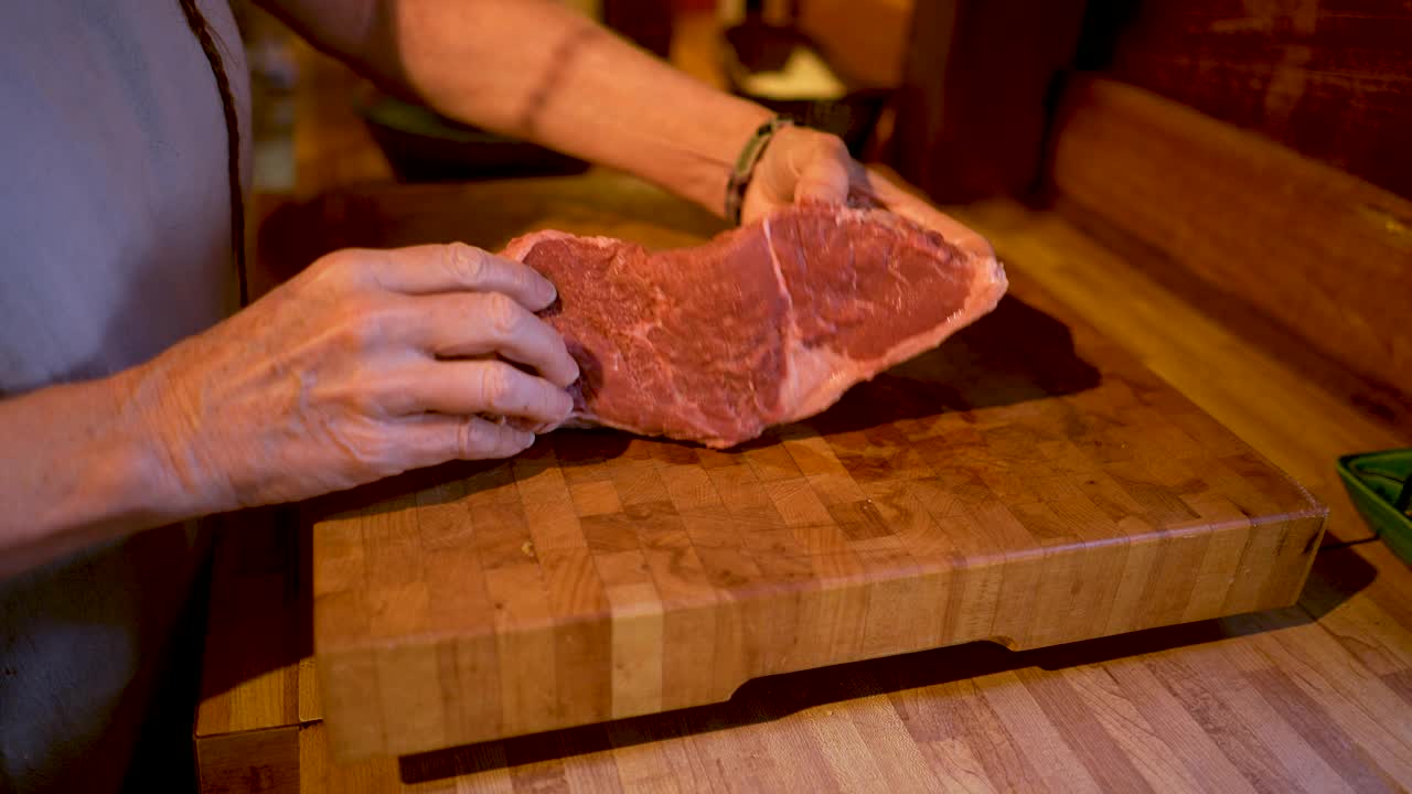 一个妇女在家里做饭，把一块牛肉放在砧板上视频下载