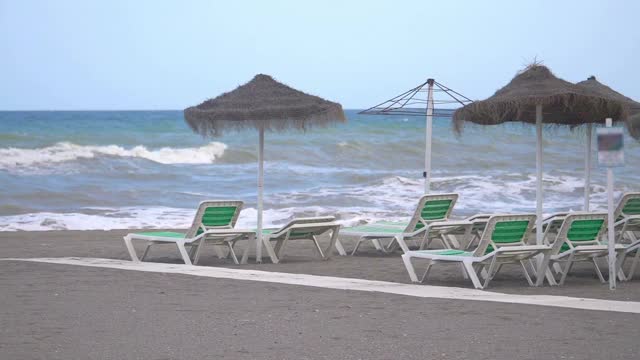 大流行期间空旷封闭的海滩上的日光浴床和遮阳伞，慢镜头180帧/秒视频素材
