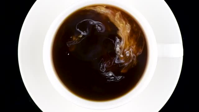 一杯咖啡俯视图。热奶油被倒入咖啡中，变成美丽的液体图案。视频素材