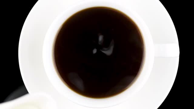 一杯咖啡俯视图。热奶油被倒入咖啡中，变成美丽的液体图案。视频素材