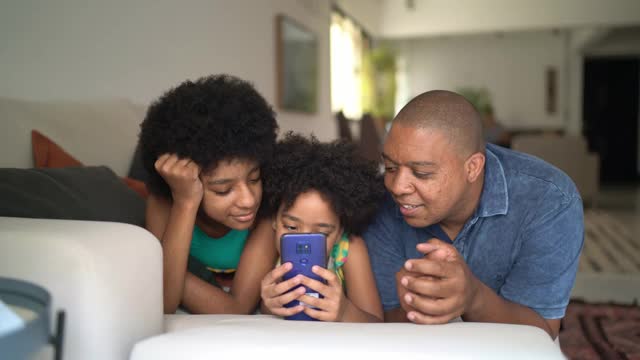 父亲和女儿一起躺在家里的沙发上使用智能手机视频素材