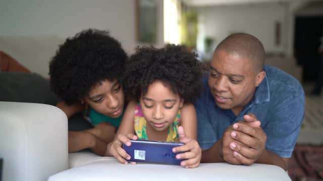 父亲和女儿一起躺在家里的沙发上使用智能手机视频下载