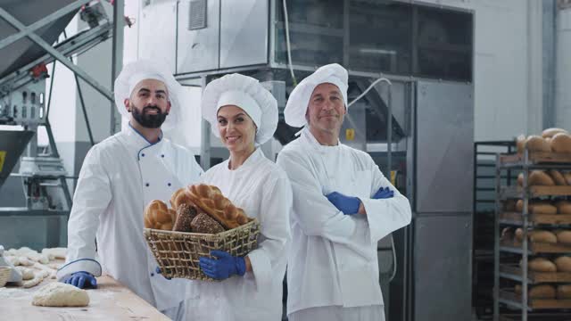 商业三个面包师的迷人的面孔肖像在一个大的面包房产业，微笑着直视着相机拿着一个有机面包的复古篮子视频素材