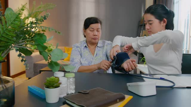 亚洲可爱的孙女在家给祖母检查血压。健康问题视频下载