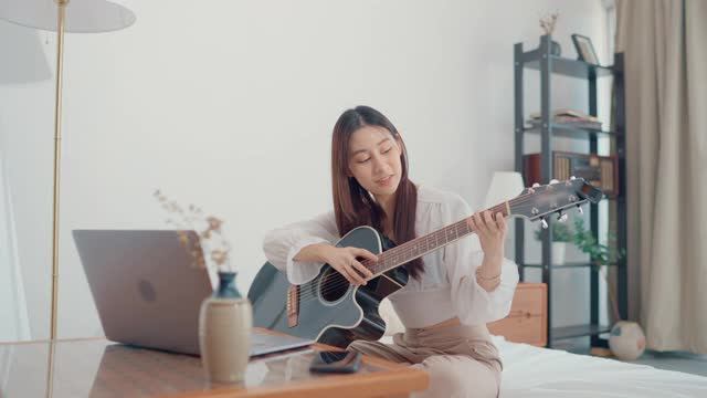 快乐的年轻女子集中学习吉他使用笔记本电脑坐在家里的客厅视频素材