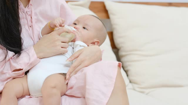 近距离的新生儿喝牛奶从瓶子和躺在他年轻的母亲在卧室的膝盖上。母亲看着她的婴儿视频素材