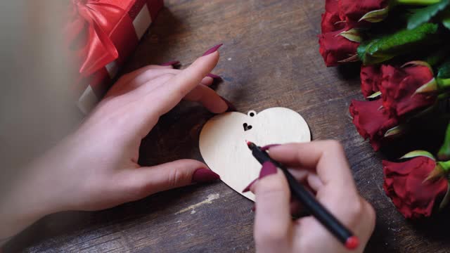 俯视图的女孩的手谁写在一个木制的心附近的一束玫瑰。情人节的概念视频素材