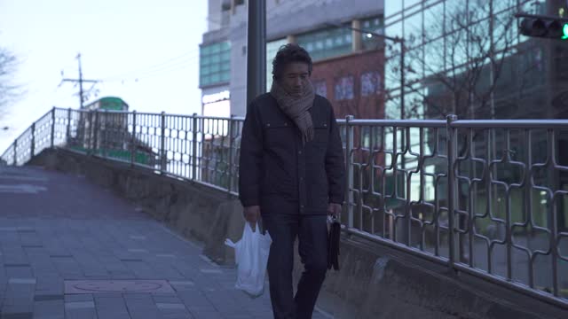 退休-中年商人独自走在大街上，手里拿着公文包和装着酒的塑料袋视频素材