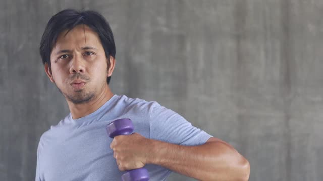 年轻的亚洲男子在健身房用哑铃锻炼视频素材