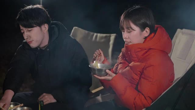 一个年轻的女人在一群朋友围坐在营火和享受食物和饮料在冬天晚上的肖像视频素材