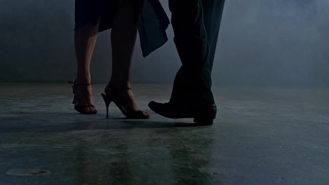 特写镜头，一名男子和一名女子在烟雾缭绕的黑暗房间里跳着拉丁舞。一个女人和一个男人的腿在黑暗的地板上美丽地跳舞。4 k, ProRes视频素材
