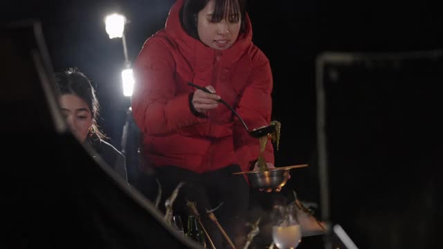 在冬天的夜晚，一群朋友围坐在营火旁，享受食物和饮料视频素材
