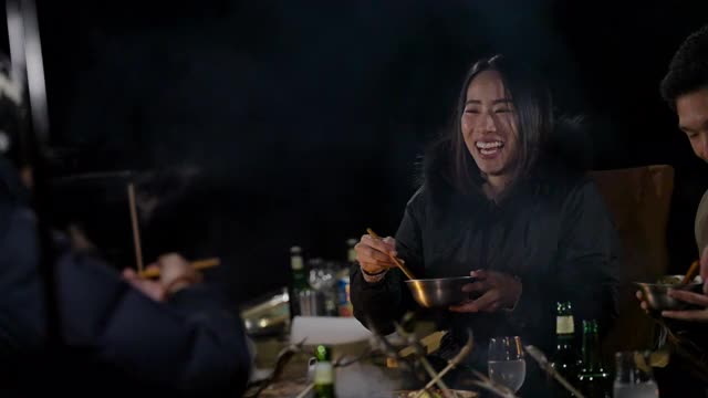 在冬天的夜晚，一群朋友围坐在营火旁，享受食物和饮料视频下载