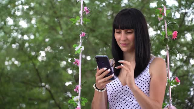 一个年轻漂亮的女孩与智能手机互动，在手机屏幕上输入文本，社交网络图标与相同的用户数量迅速增加视频素材