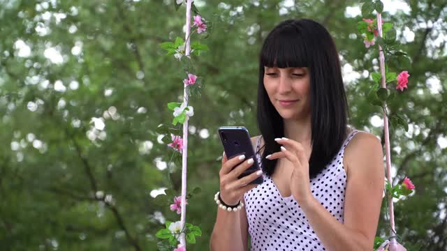 一个年轻漂亮的女孩与智能手机互动，在手机屏幕上输入文本，社交网络图标与相同的用户数量迅速增加视频下载