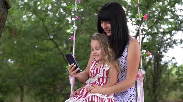 一位带着孩子的年轻女性使用手机，用智能手机在社交网络上创建用户界面——点赞、关注者和评论。视频素材
