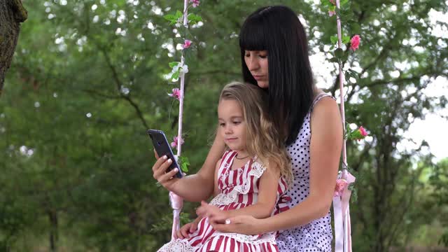 一位带着孩子的年轻女性使用手机，用智能手机在社交网络上创建用户界面——点赞、关注者和评论。视频下载
