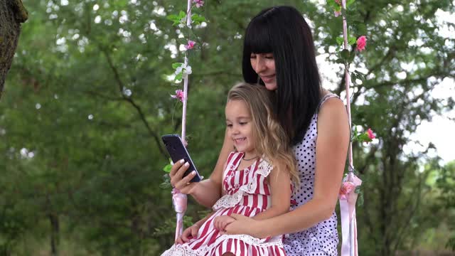 一位带着孩子的年轻女性使用手机，用智能手机在社交网络上创建用户界面——点赞、关注者和评论。视频下载