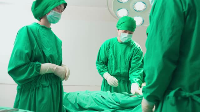 专业的医疗团队在现代化的手术室里进行外科手术。在医院重症监护病人做手术时，亚洲助手向外科医生分发器械。视频素材