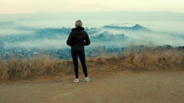 正在上升的无人机拍摄的女子看在雾蒙蒙的景色视频素材
