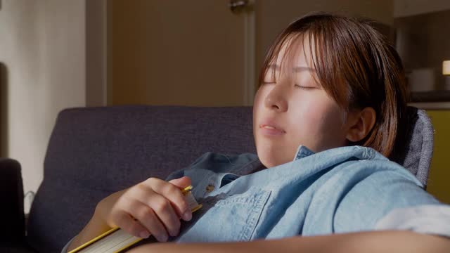 年轻女子舒适地睡在沙发上，而拿着书在客厅在家里视频素材