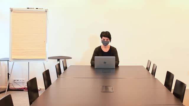 一位戴面具的女士坐在桌边用笔记本电脑解决工作问题。视频素材