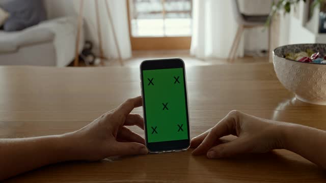 一个无法识别的人使用带有色度键绿色屏幕的智能手机视频素材