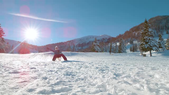 镜头光晕:快乐的白种女人骑着木制雪橇从雪山上飞驰而下。视频素材